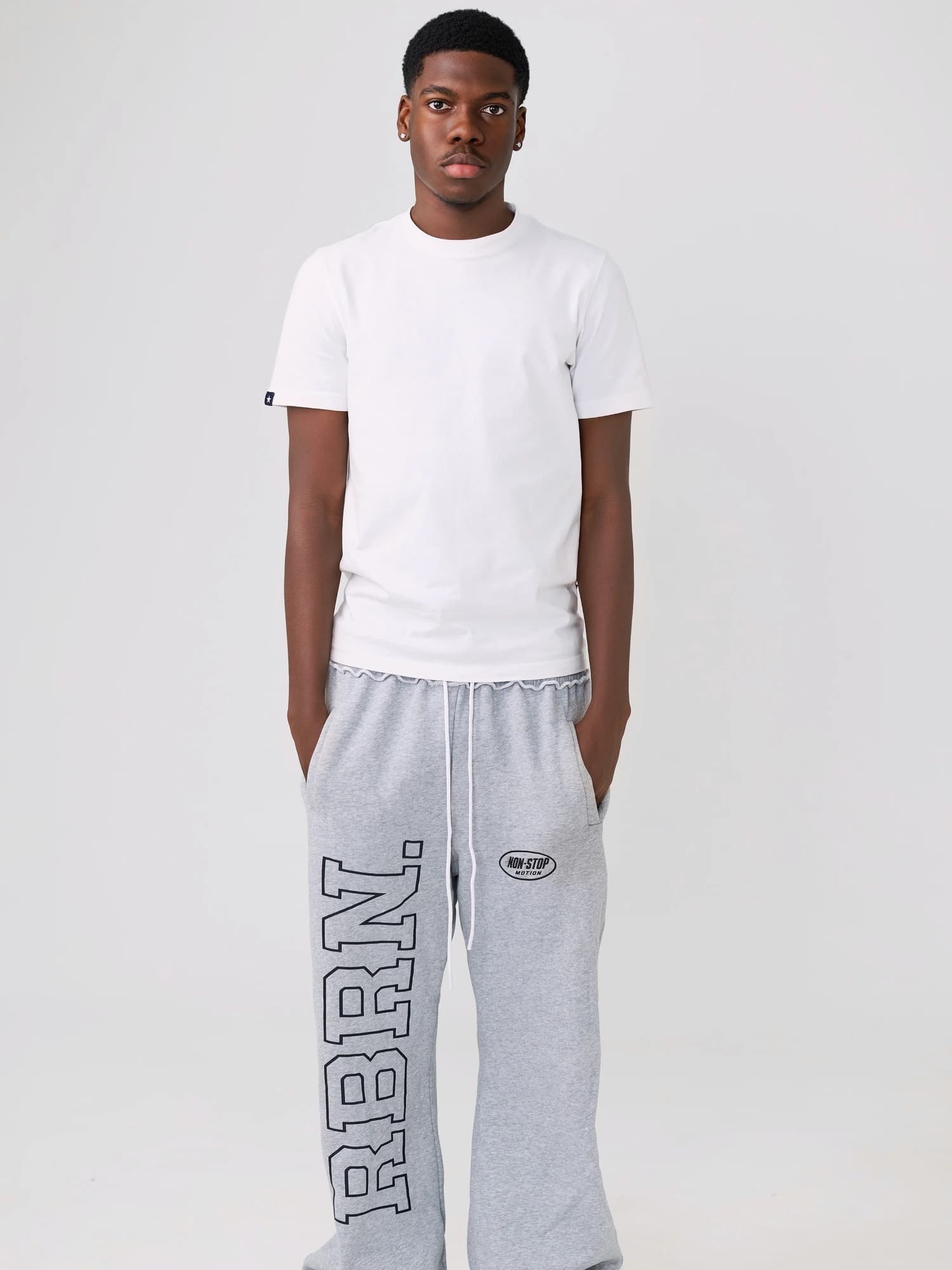 Studio portrait of a man in a white T-shirt and grey trousers against a pale backdrop.