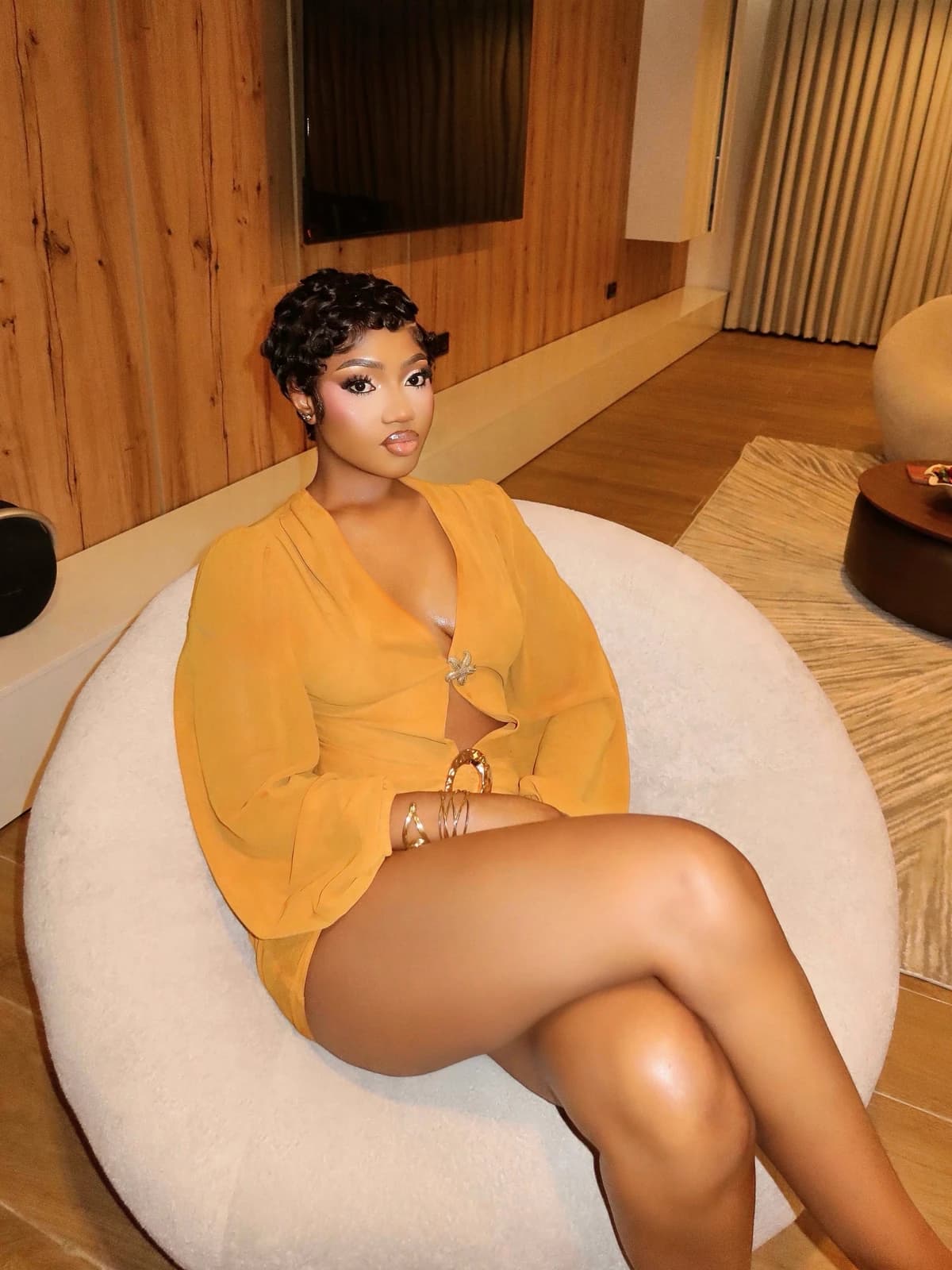 Portrait of a woman in a mustard outfit seated in an ivory armchair.